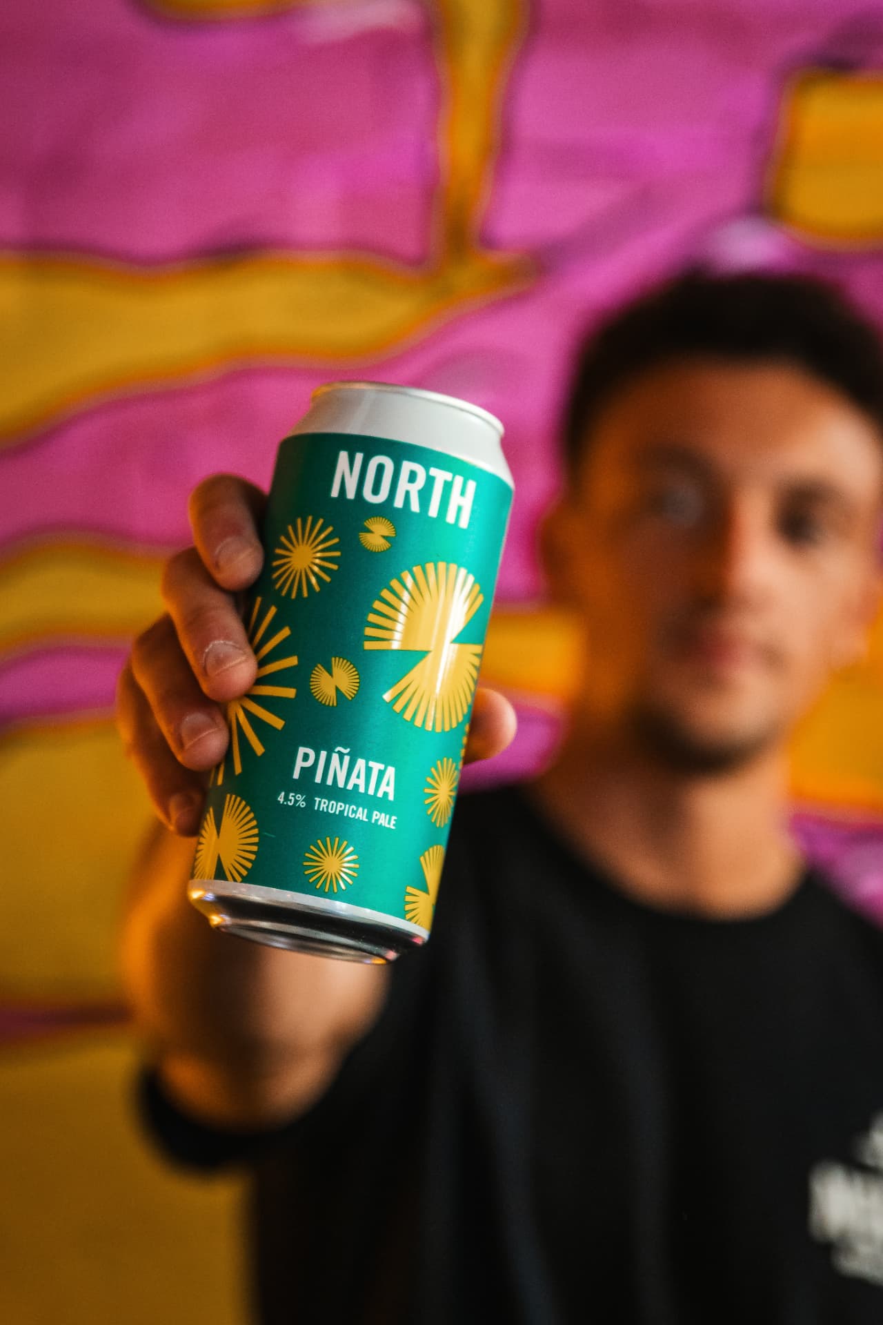 North Brewing Piñata tropical pale can held against a mural