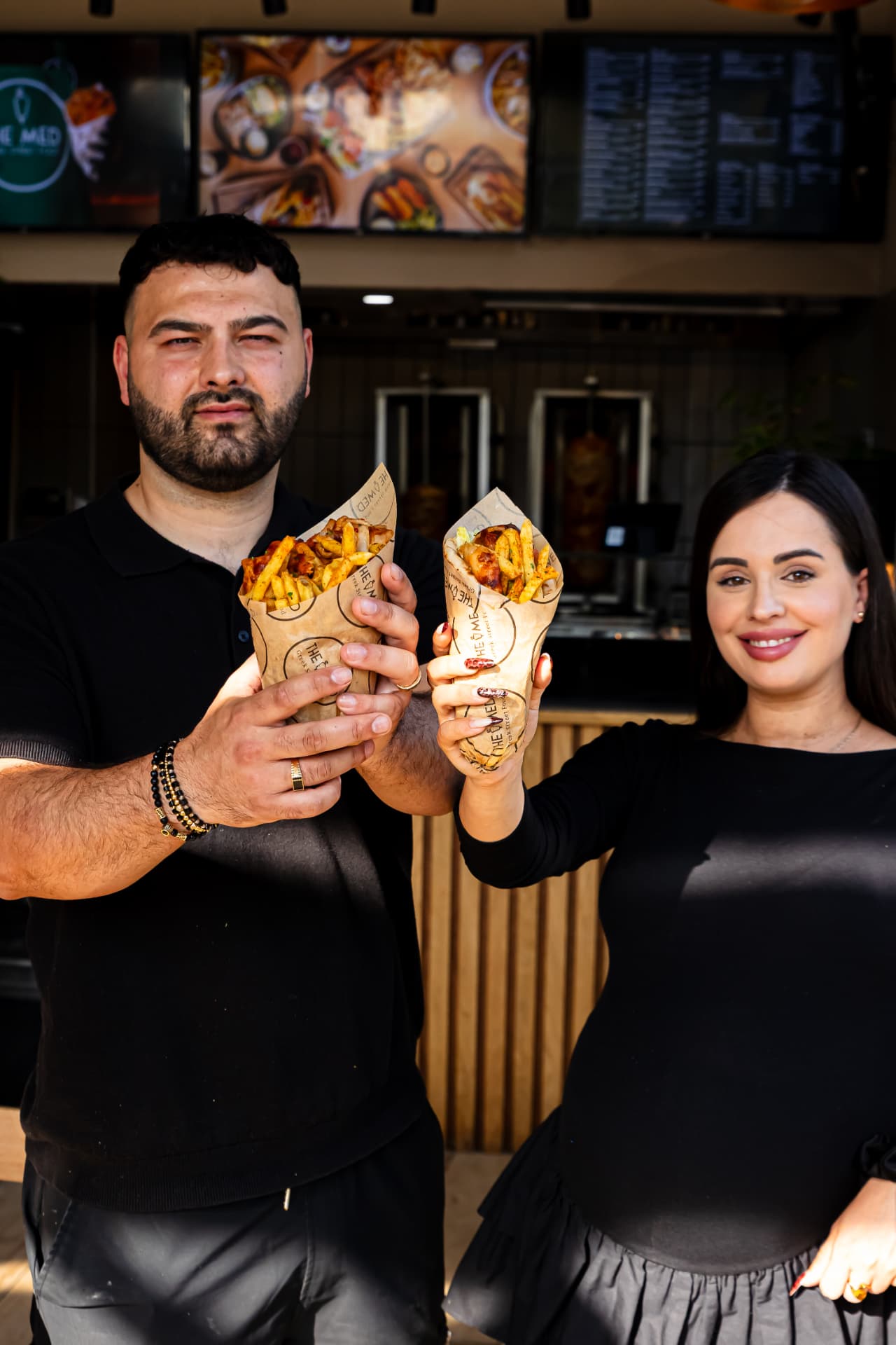 Owners holding gyros wraps outside a Greek street food shop